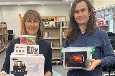 Two library staff members holding up tech items for loan