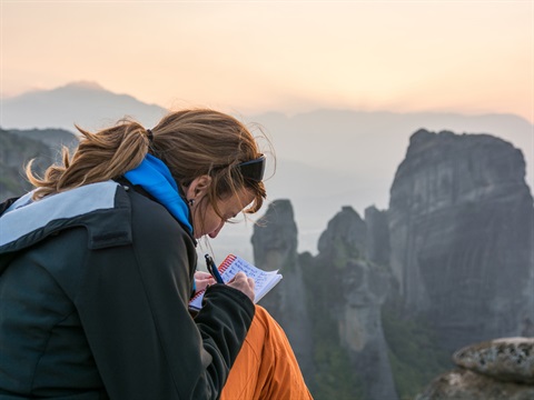 person writing sitting on a cliff