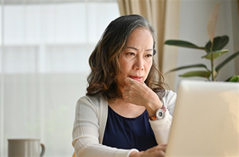 Older woman sitting at table with laptop, focused on screen.