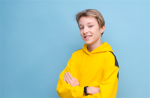 A happy boy in a yellow hoodie, smiling brightly against a vibrant blue background.