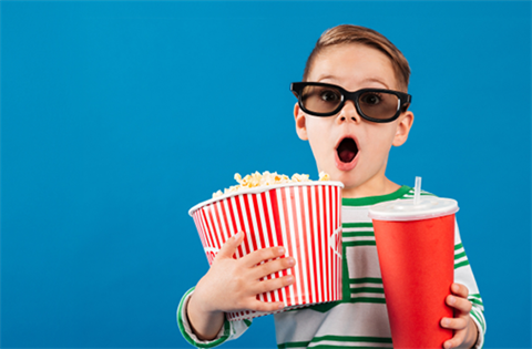 A young boy in 3D glasses enjoying a movie night with a bucket of popcorn and a drink.