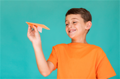 Child in an orange tshirt holding a paper plane