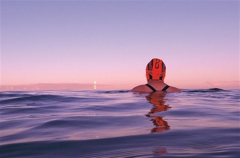 A person sitting in the ocean at sunrise